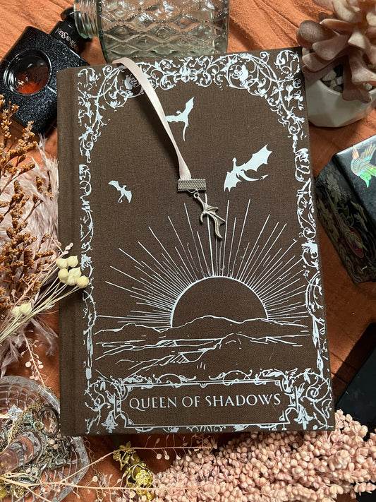 Queen of Shadows rebind with brown book cloth and silver foiled vinly. Shows sun in clouds and wyvrens flying above